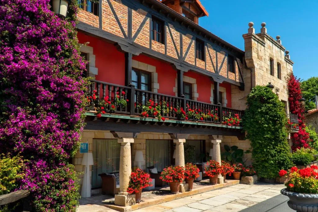 Fachada de piedra y entramado de madera de Costa Esmeralda Suites en el casco histórico de Suances, con balcón lleno de geranios y buganvilla