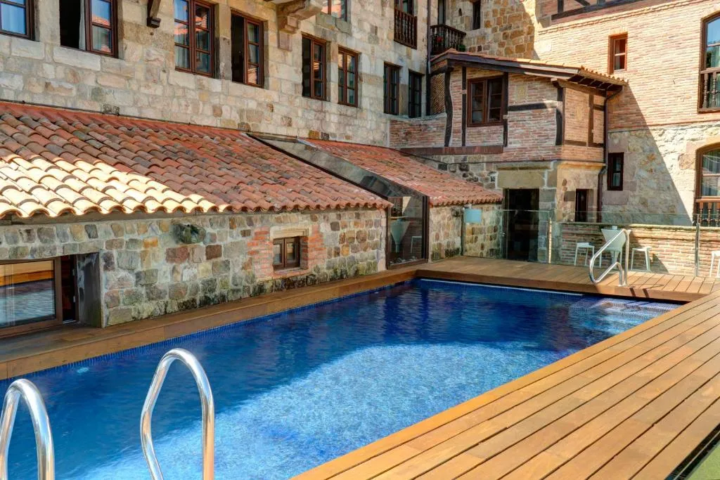 Piscina exterior climatizada junto a la fachada de piedra centenaria del hotel, con solárium de madera