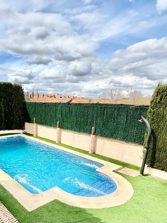 Piscina azul rodeada de seto y un cielo con nubes