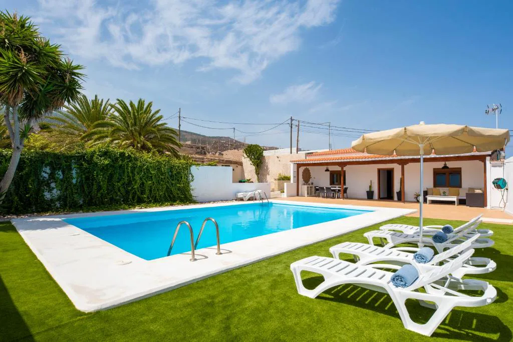 Piscina rodeada de césped artificial y palmeras junto a la casa blanca, Eco-Finca Güímar
