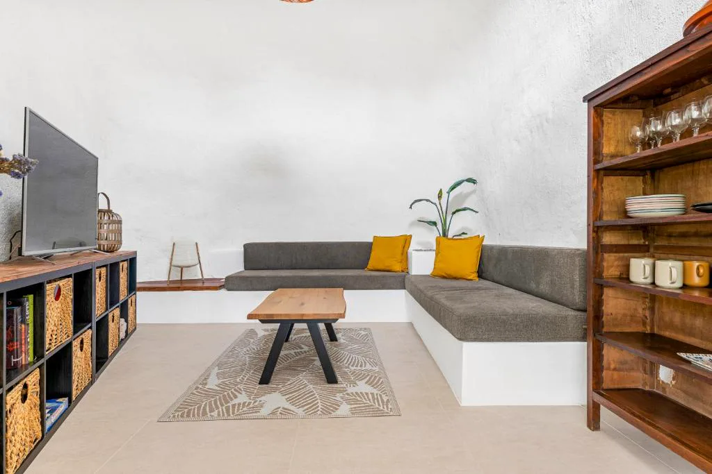 Salón con sofá gris y cojines mostaza junto a estantería de madera, Eco-Finca Güímar