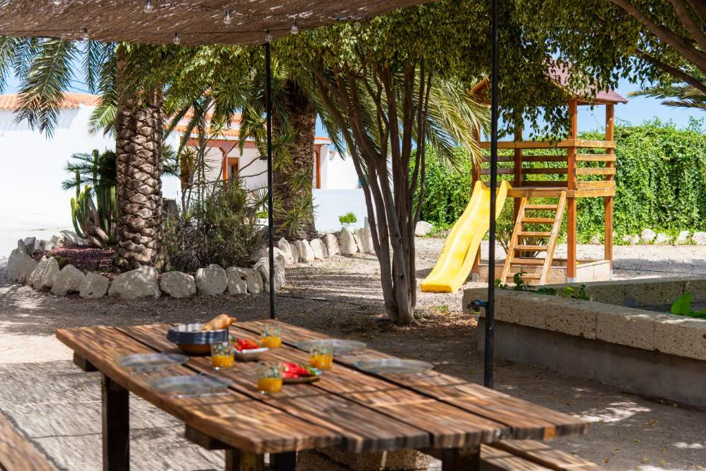 Mesa de picnic bajo los árboles junto a un tobogán infantil en el jardín, Eco-Finca Güímar
