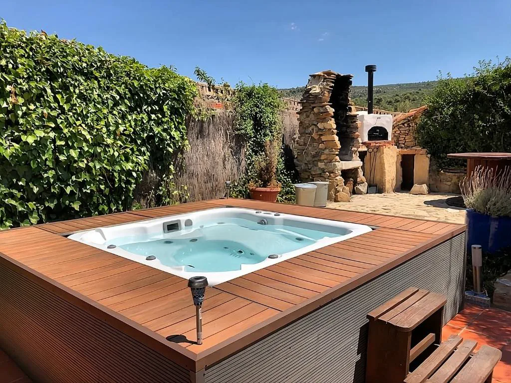 Jacuzzi de madera en un patio con muro de piedra y flores