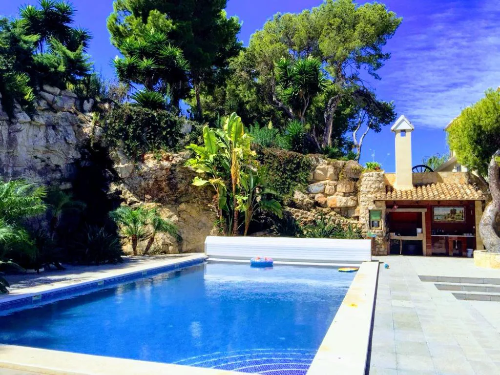 Piscina azul entre vegetación con un cenador al fondo