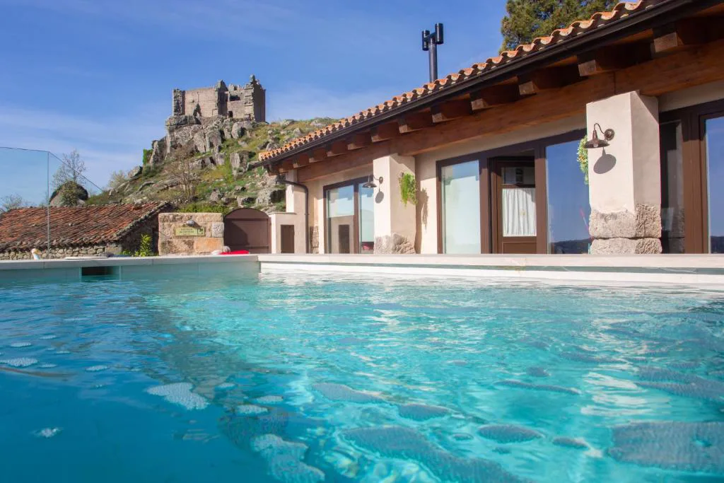Piscina turquesa junto a una casa de piedra con vistas al castillo