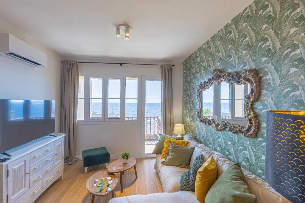 Salón con papel pintado botánico verde y sofá junto al balcón al mar, El Mirador de Julia