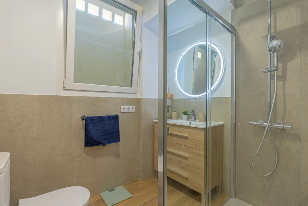 Baño con espejo circular retroiluminado y mueble de madera, El Mirador de Julia
