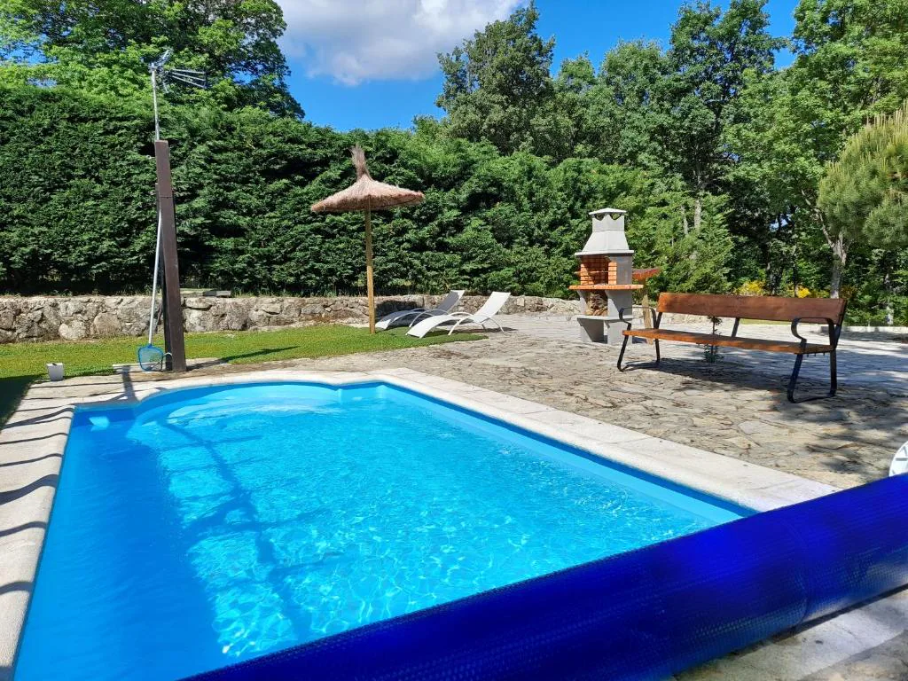 Piscina con sombrilla, barbacoa y banco entre árboles