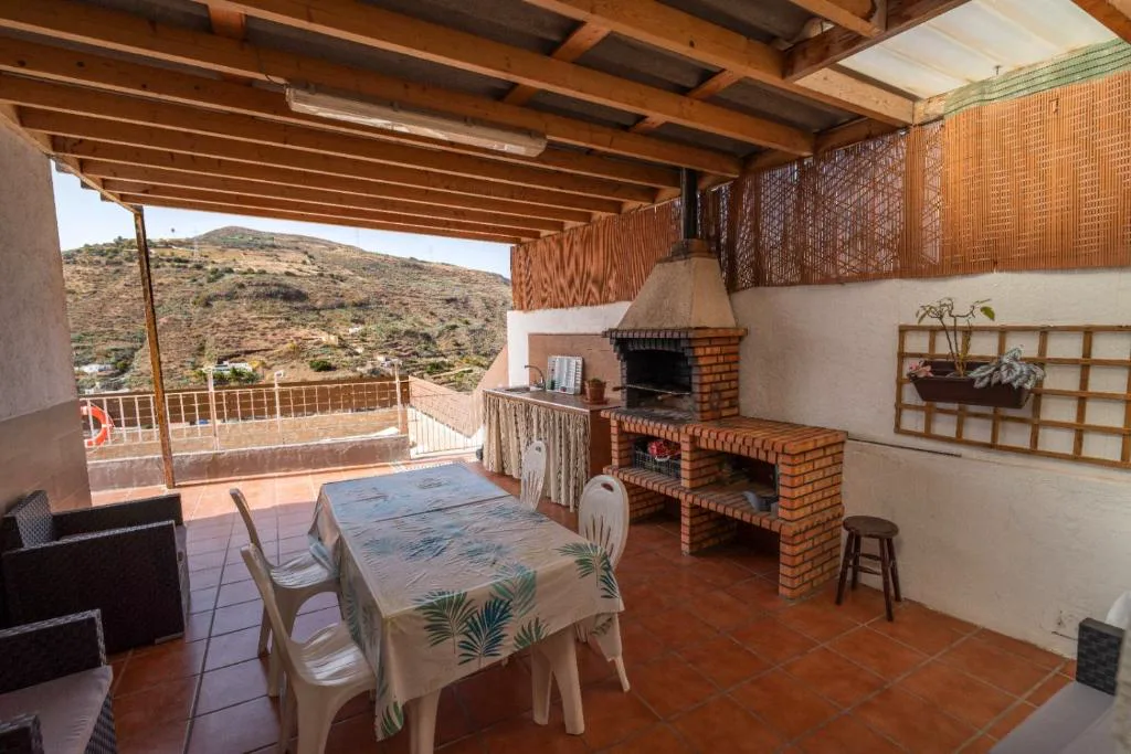 Terraza cubierta con barbacoa de obra y mesa junto a vistas al valle, El Recoveco de La Solana