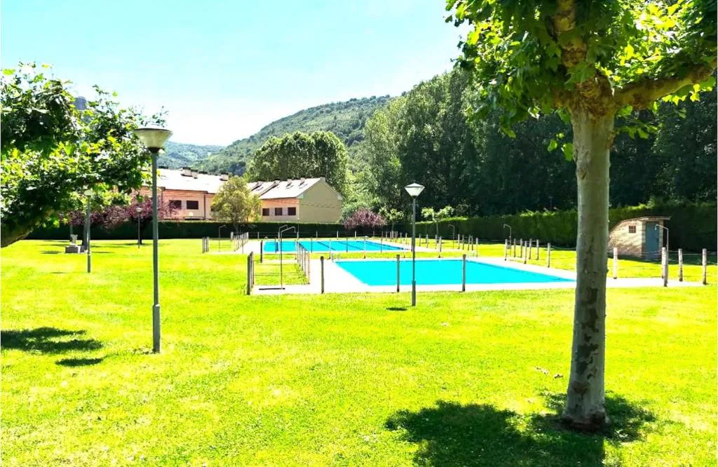 Piscina azul en un césped verde con montañas al fondo