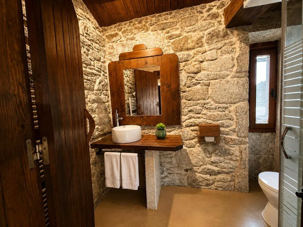 Baño rústico con lavabo de madera y paredes de piedra, Elemergia