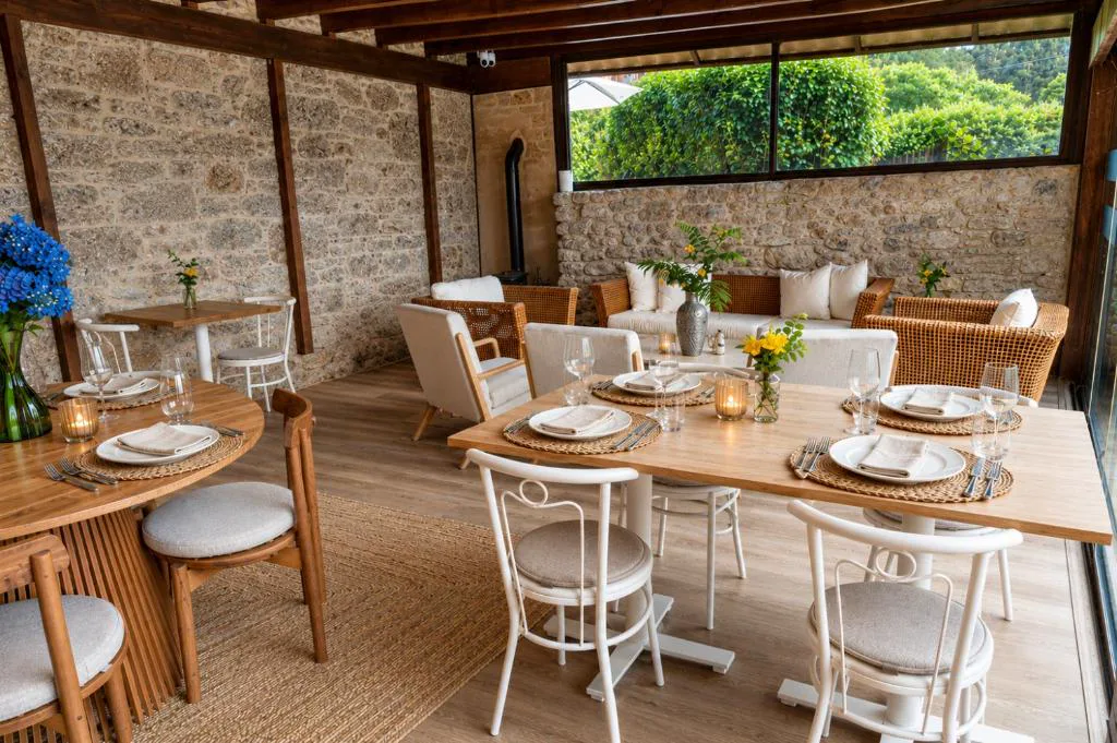 Comedor bajo pérgola de madera con chimenea y mesas puestas, Elemergia