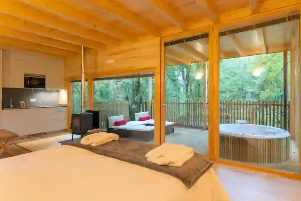 Cama frente a la terraza acristalada con bañera de hidromasaje exterior entre los árboles