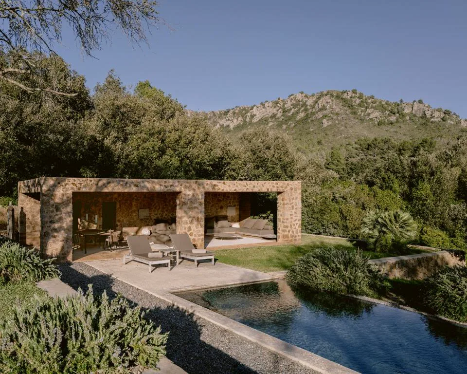 Pabellón de piedra junto a la piscina con sofás bajo un porche de tres arcos, Es Racó d'Artà