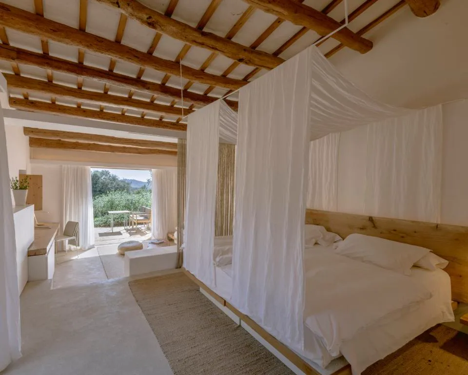 Dormitorio con cama de dosel de lino blanco bajo techo de vigas de madera, Es Racó d'Artà