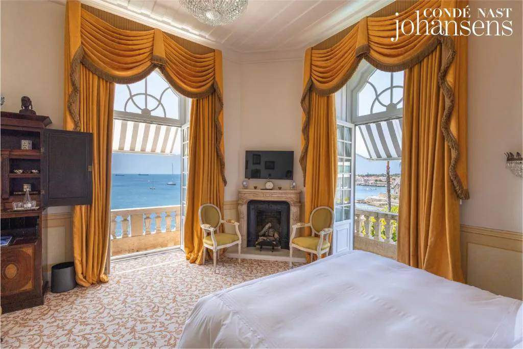 Habitación con cortinas doradas y balcón abierto al mar, Estoril Vintage Hotel