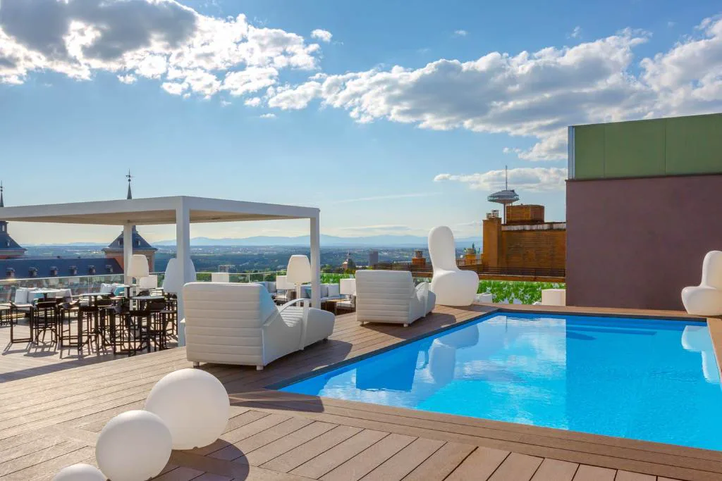 Piscina de azotea con sombrillas blancas y sofás bajo el cielo azul