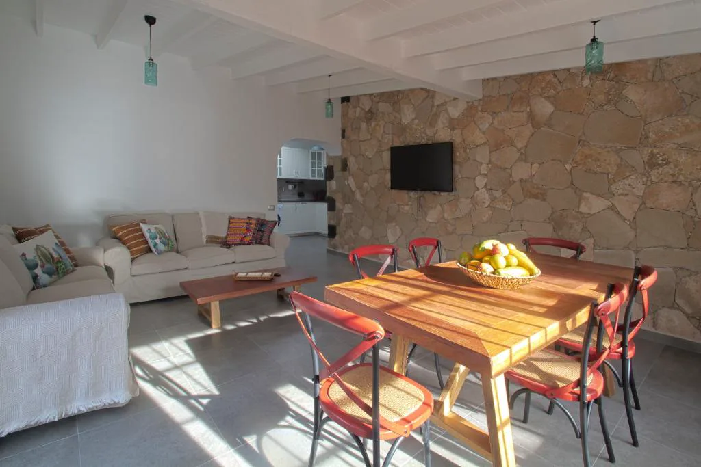 Comedor con pared de piedra vista, mesa de madera maciza y sillas rojas de rejilla, Finca Arbequina