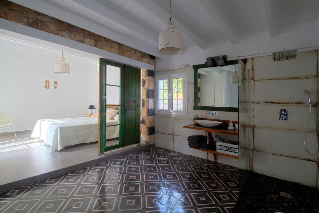 Dormitorio con puerta verde antigua abierta a un baño industrial con lavabo de madera, Finca Arbequina