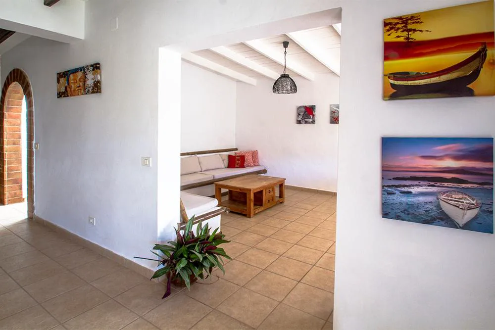 Salón luminoso con sofás blancos y cuadros de barcos al atardecer, Finca Arbequina