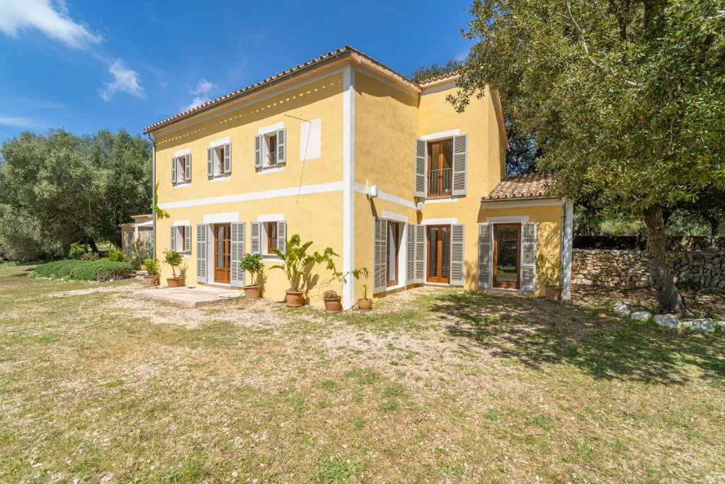 Fachada trasera de la finca amarilla con contraventanas grises y jardín, Can Regalat