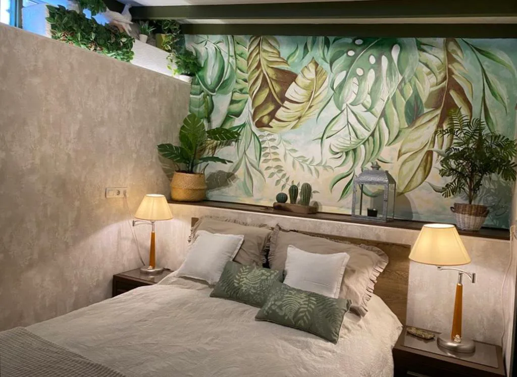 Dormitorio con mural pintado de hojas tropicales y lámparas de mesa naranjas, Finca Cebollino