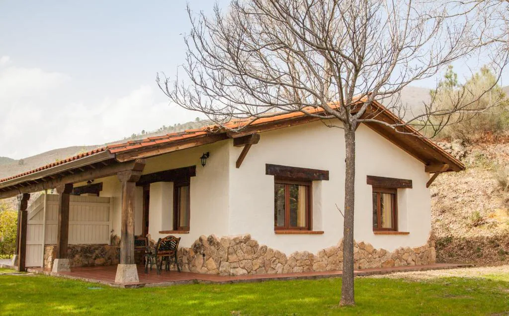 Casita blanca de teja con porche entre césped y árboles