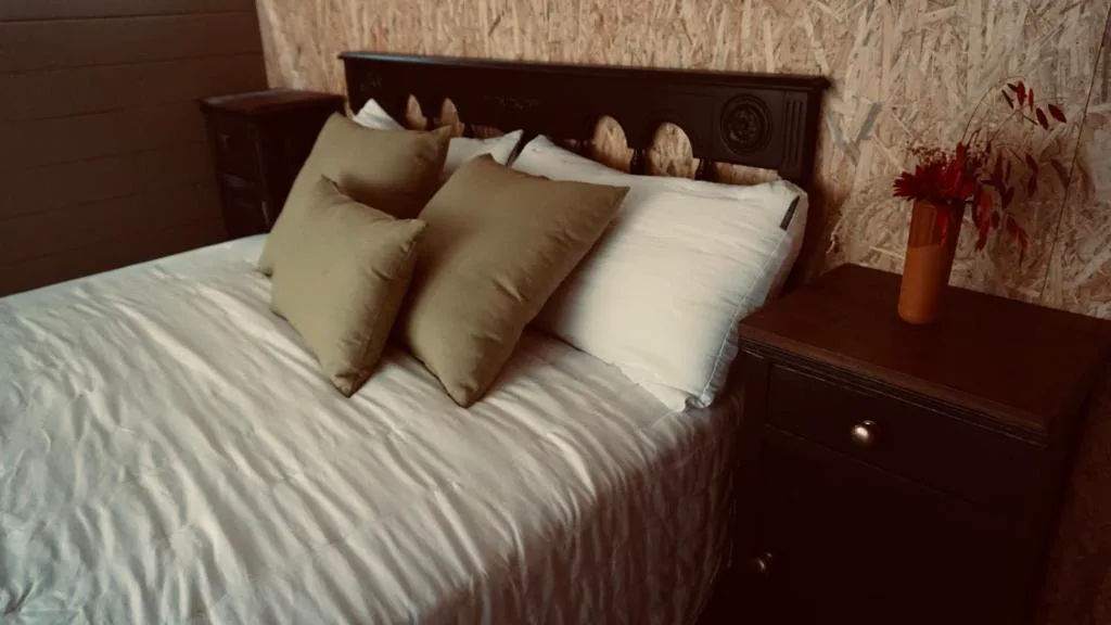 Dormitorio con cojines verde oliva y mesita de noche oscura, Cabañas Finca Real