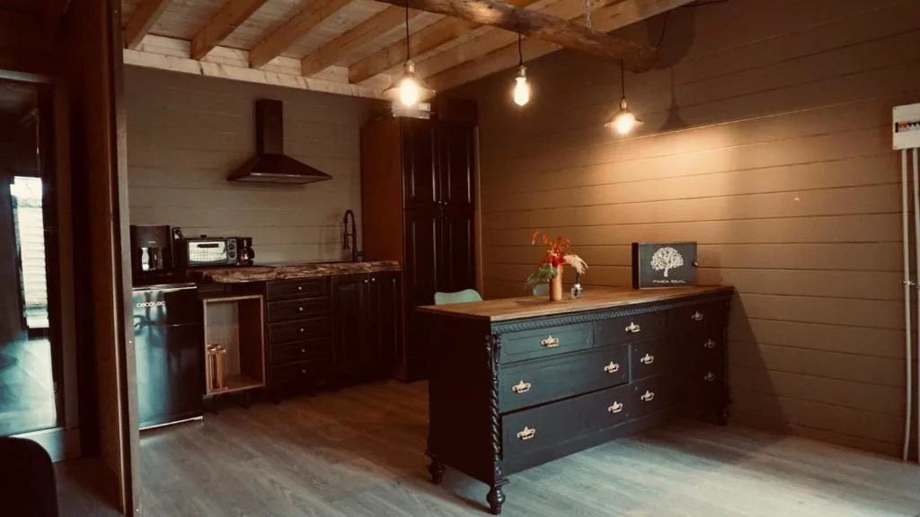 Cocina con isla de madera oscura y letrero Finca Real, bajo vigas vistas