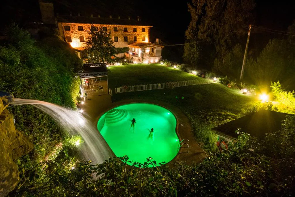 Piscina iluminada de verde con cascada al anochecer