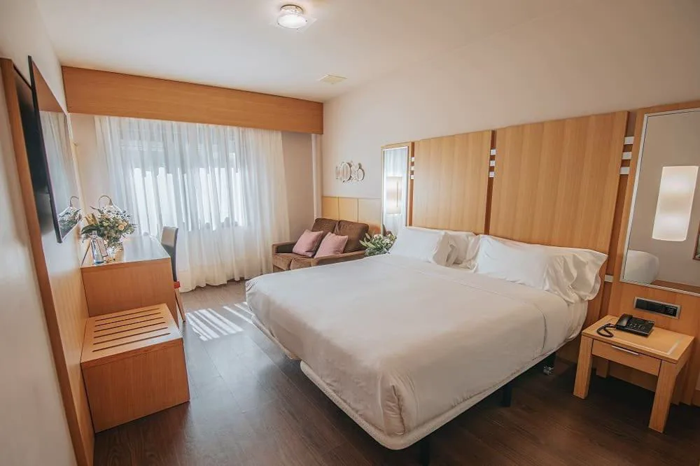 Habitación luminosa con cabecero de madera y sofá junto a la ventana, Gran Talaso Hotel Sanxenxo
