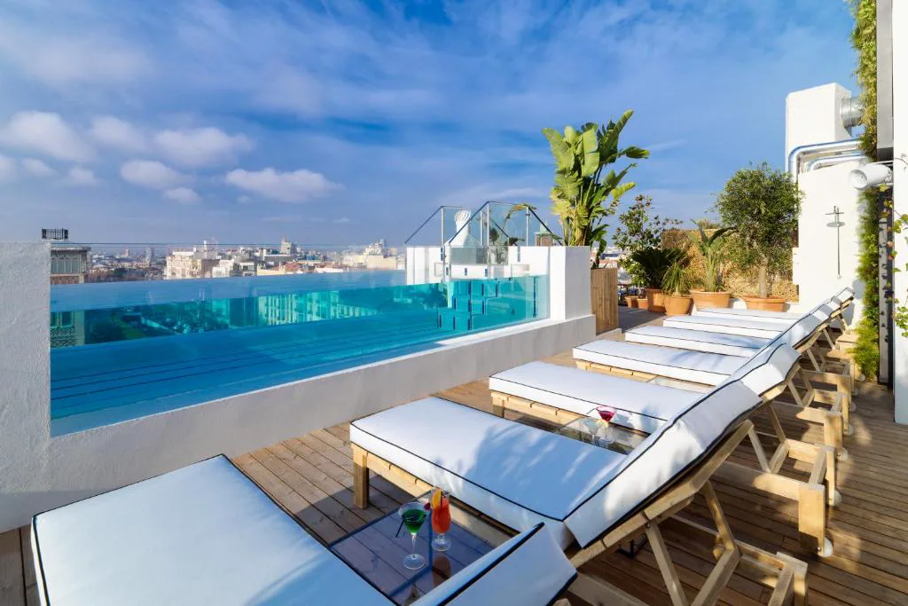 Piscina de azotea con lateral de cristal, tumbonas y vistas al centro de Madrid