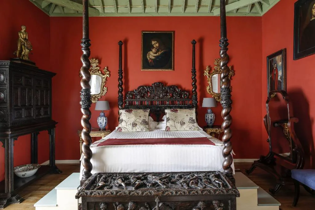 Dormitorio de paredes rojas con cama de dosel y antigüedades, Hacienda de Abajo