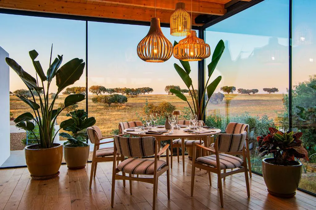 Mesa puesta en el restaurante acristalado con vistas a la llanura al atardecer, Herdade da Malhadinha Nova