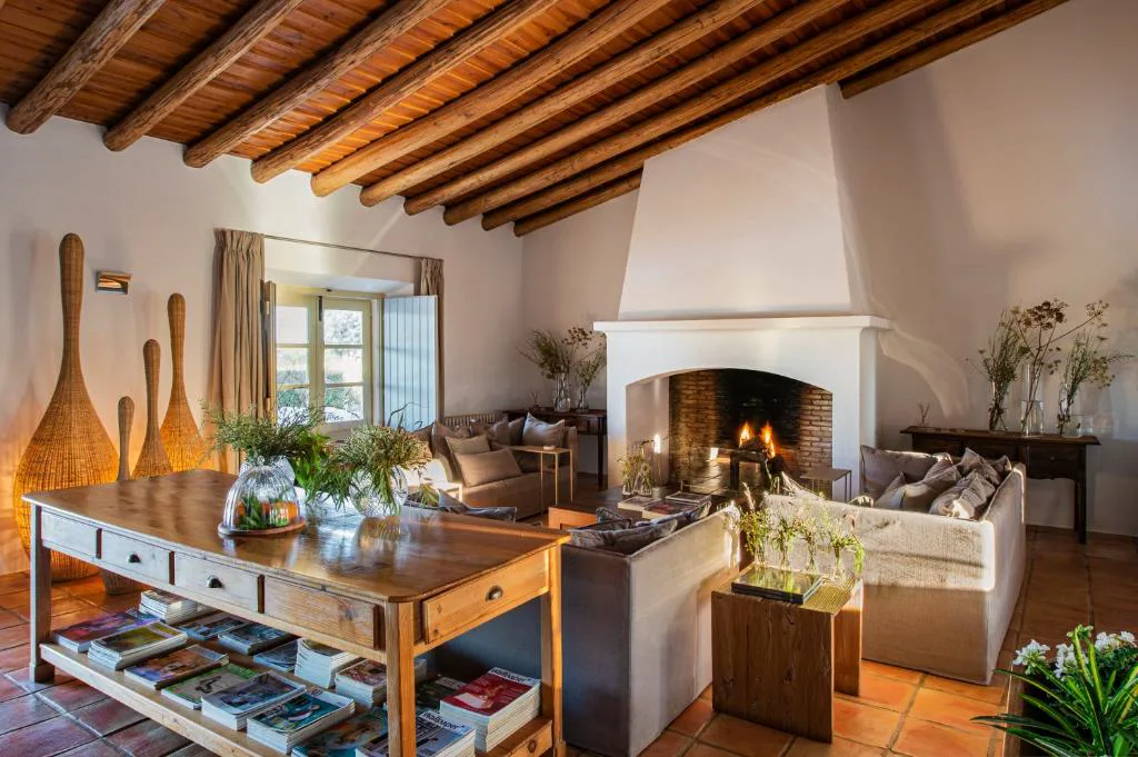 Salón rústico con chimenea encendida y techo de vigas de madera, Herdade da Malhadinha Nova