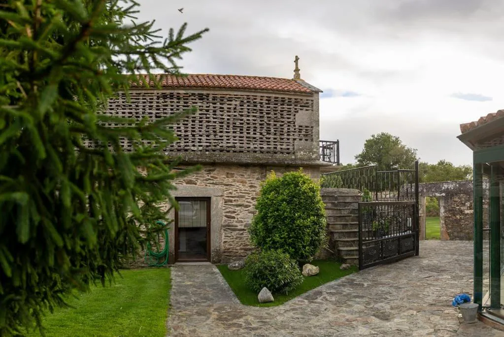 Detalle de la celosía de piedra tradicional del hórreo restaurado, con jardín y verja de acceso