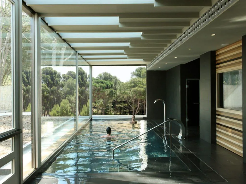 Piscina interior de spa con cristaleras abiertas al pinar