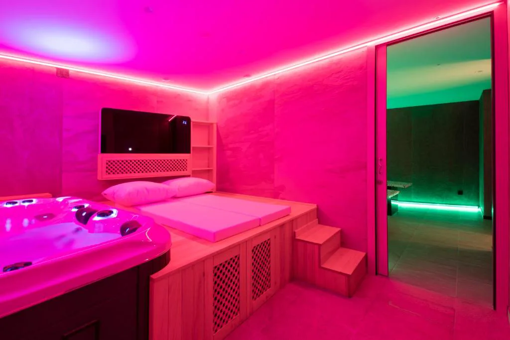 Sala de spa con jacuzzi y luz rosa junto a una sauna verde