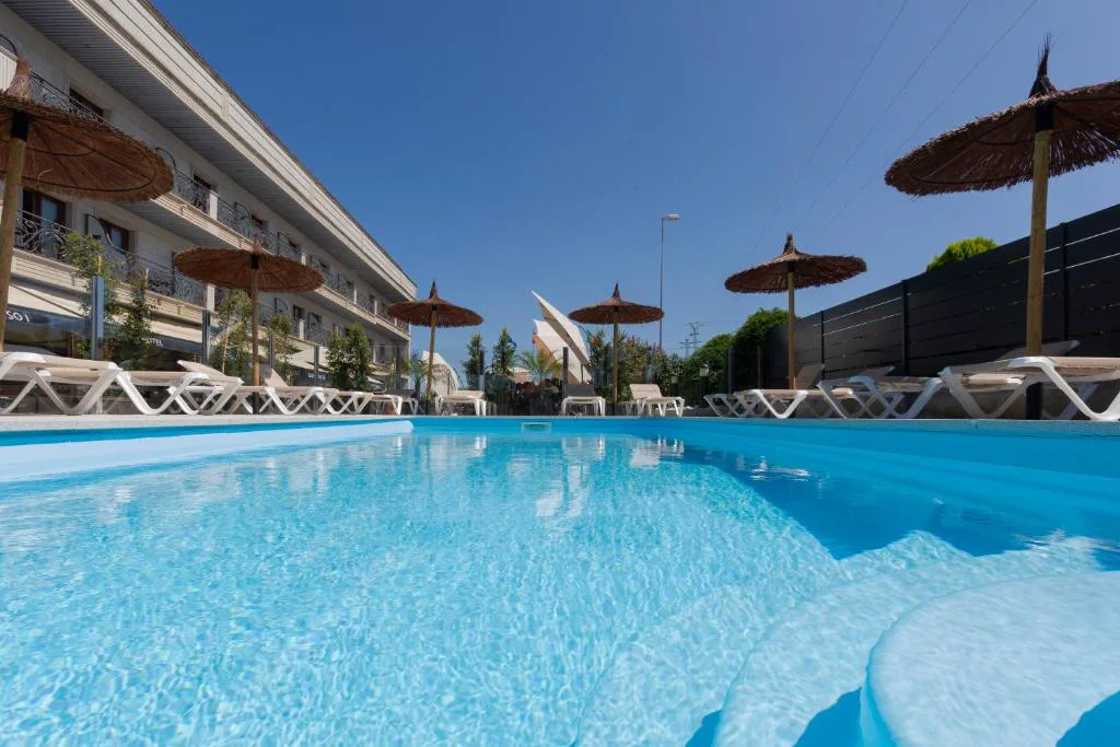 Piscina exterior con sombrillas de fibra natural junto a la fachada del hotel, Hotel Alfonso I