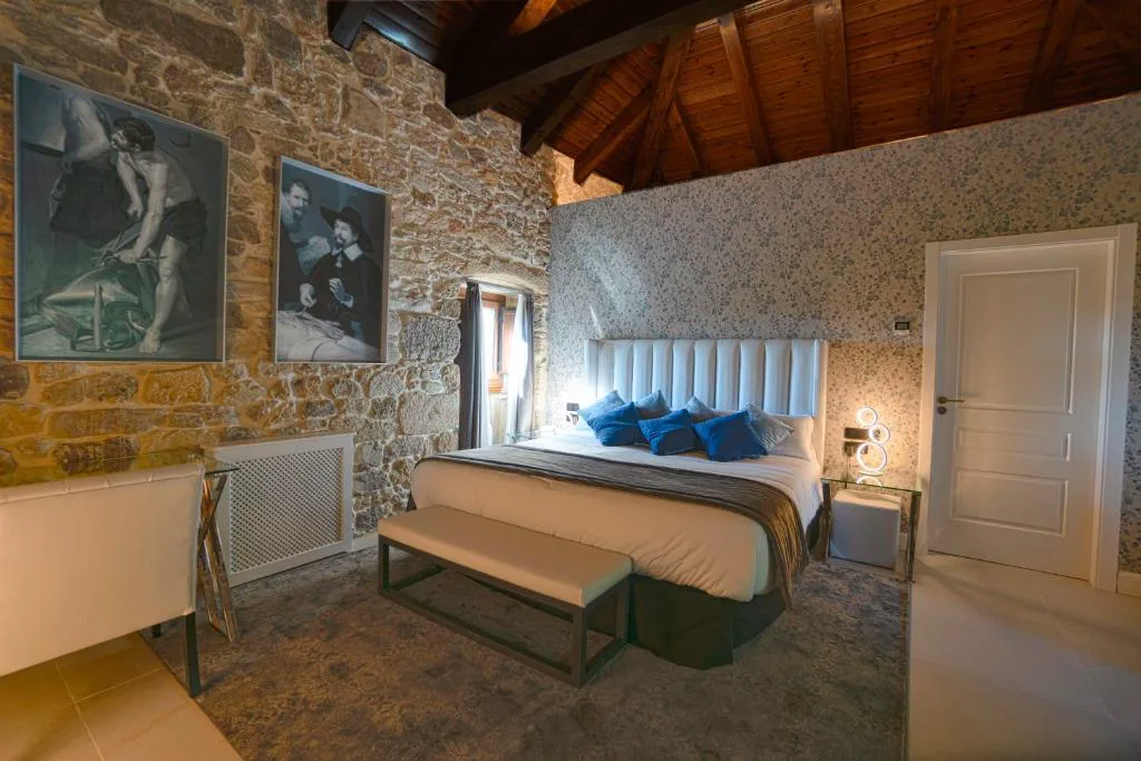 Habitación con cabecero capitoné y cuadros clásicos sobre pared de piedra, Hotel As Torres da Hermida