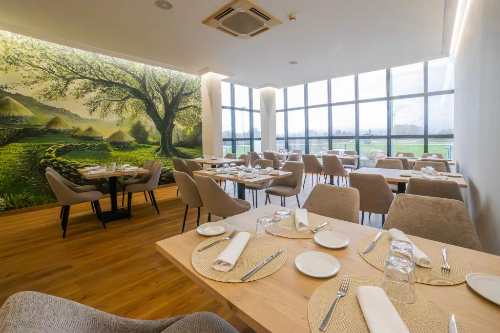 Comedor del restaurante con mesas puestas y mural de paisaje verde, Hotel Auditorio Santiago & Spa