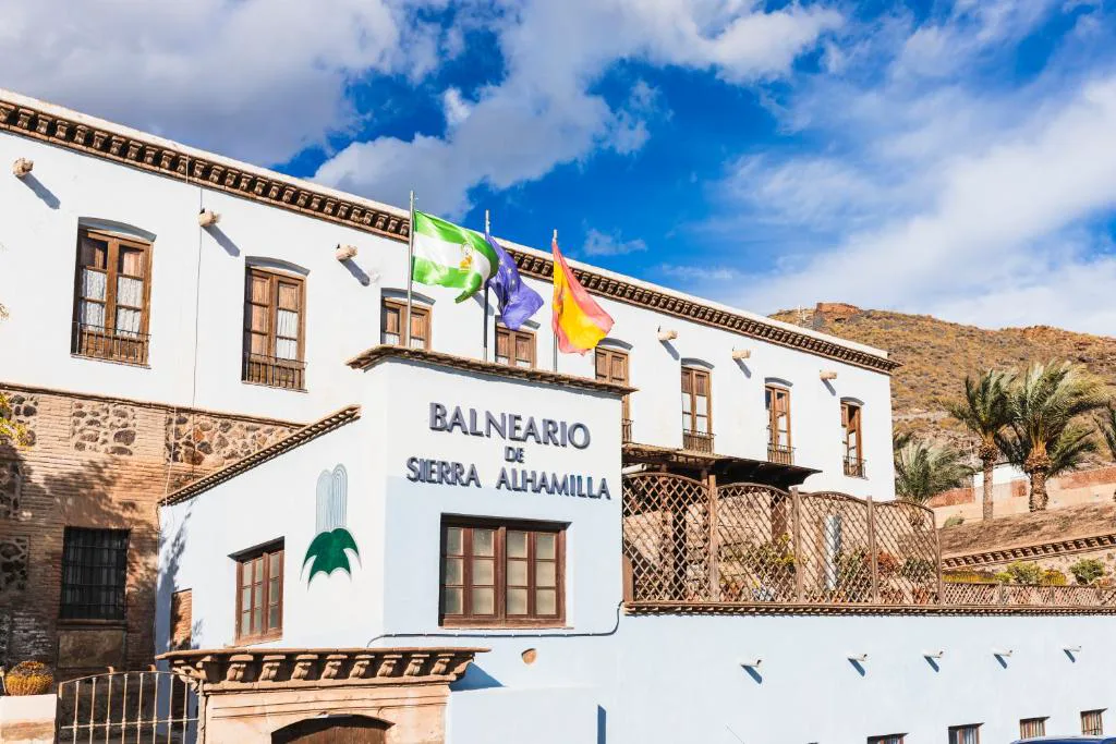 Fachada blanca del balneario con banderas y palmeras
