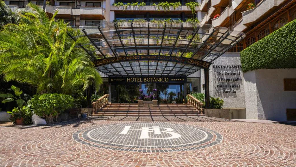 Entrada principal del hotel bajo pérgola acristalada con jardín tropical, Hotel Botanico