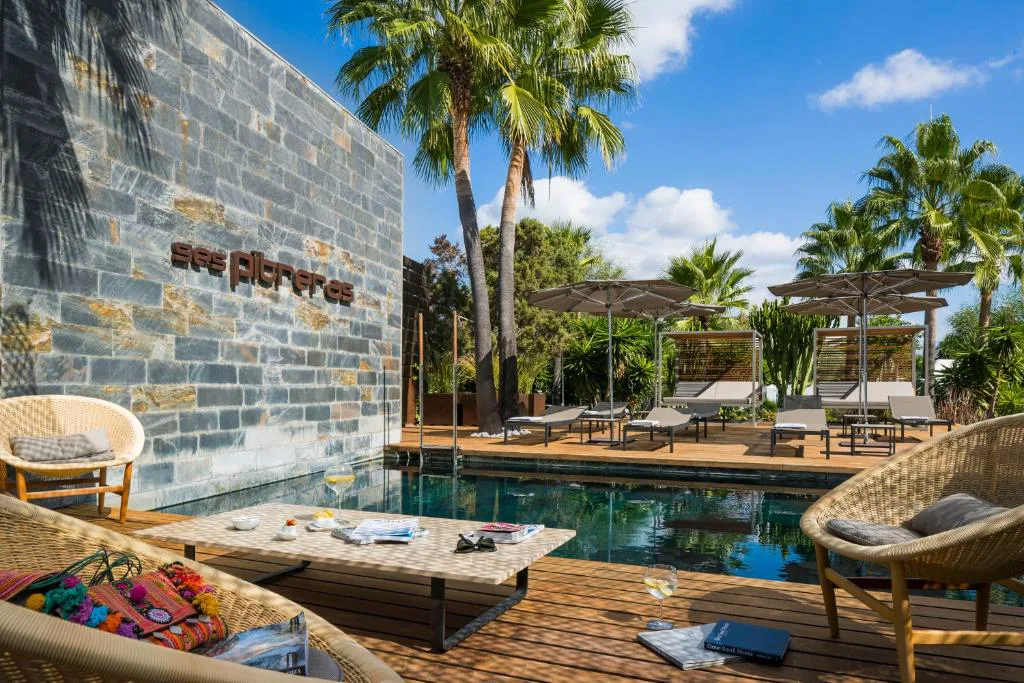 Piscina exterior con tumbonas y sombrillas junto al logo del hotel en piedra, Ses Pitreras