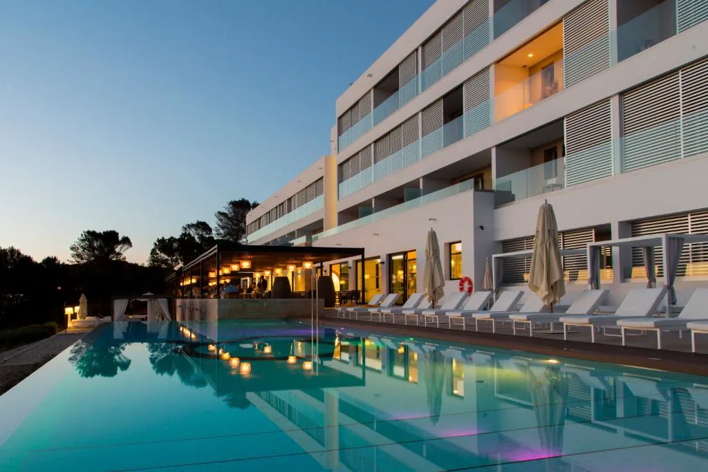 Piscina iluminada al atardecer junto a la fachada del hotel, Hotel Cala Saona & Spa