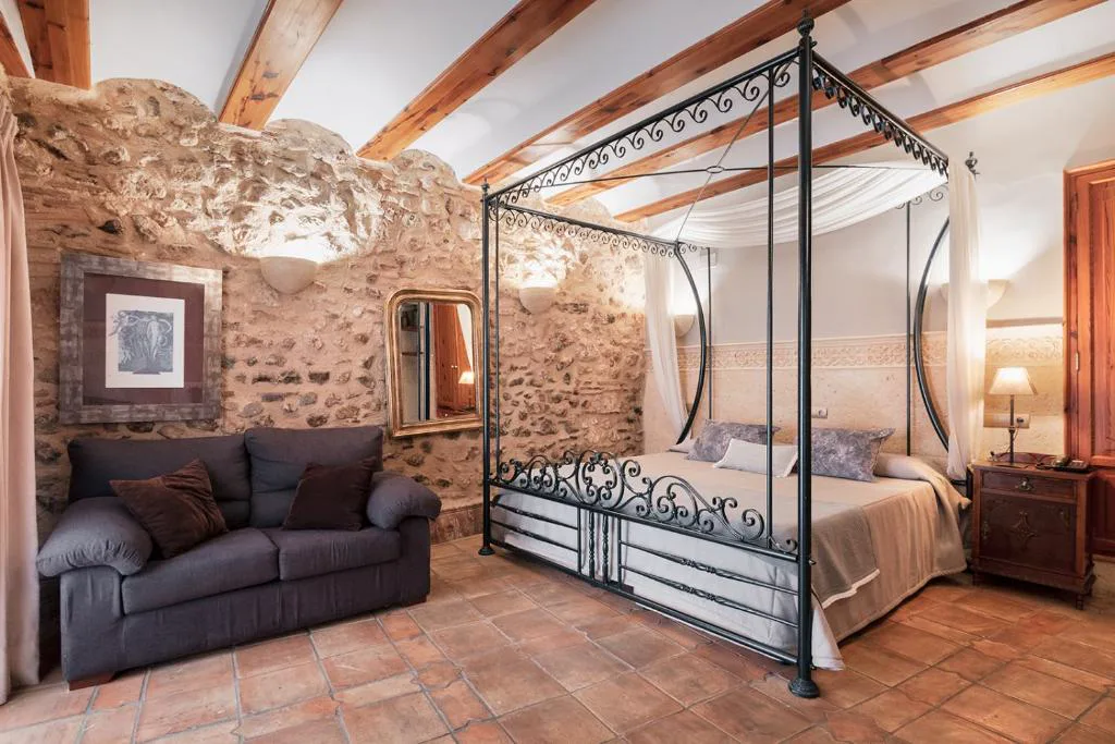 Habitación con cama con dosel de forja y pared de piedra