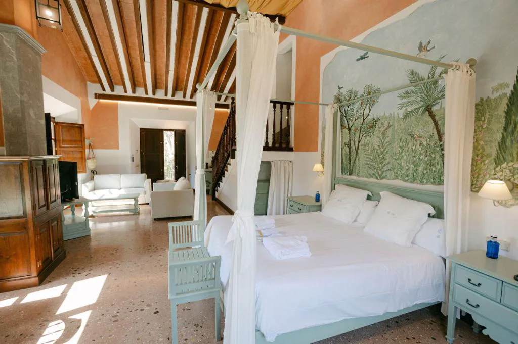 Dormitorio con cama con dosel de tela blanca y mural pintado de bosque mediterráneo, Hotel Finca Ca N'ai