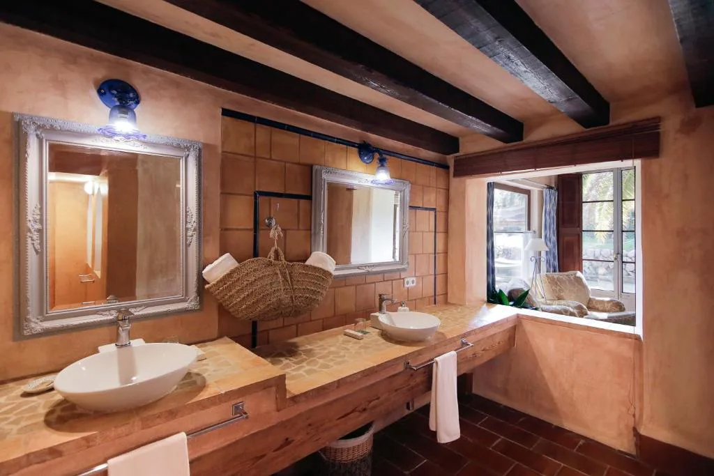 Baño con doble lavabo de piedra tallada y vigas de madera oscura, Hotel Finca Ca N'ai