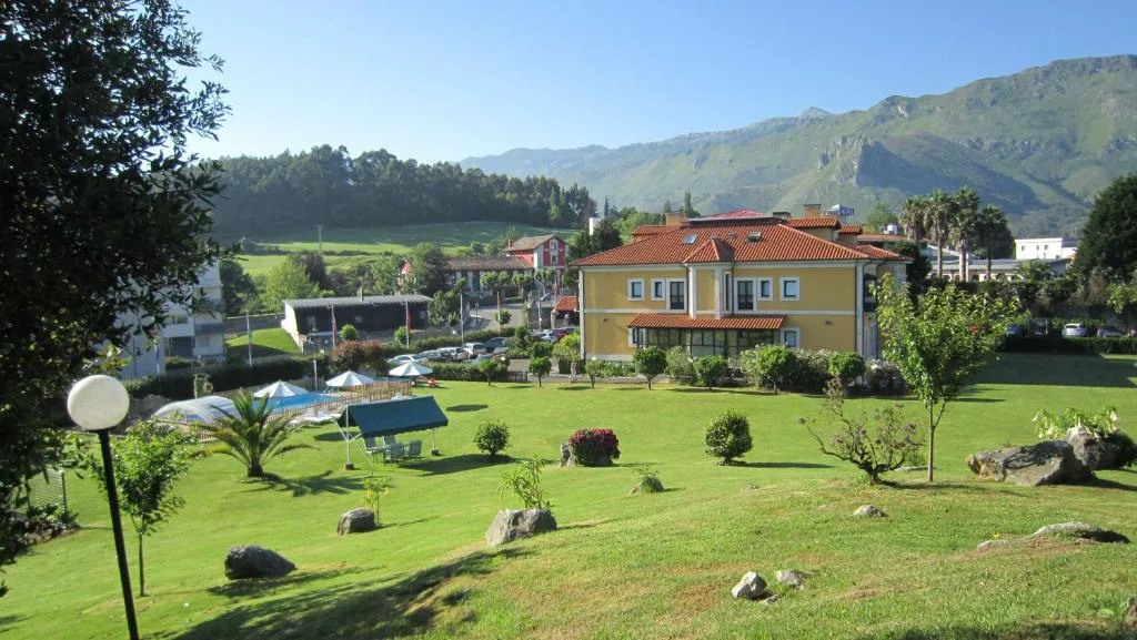 Jardín con farolas y el hotel de fondo con las montañas detrás