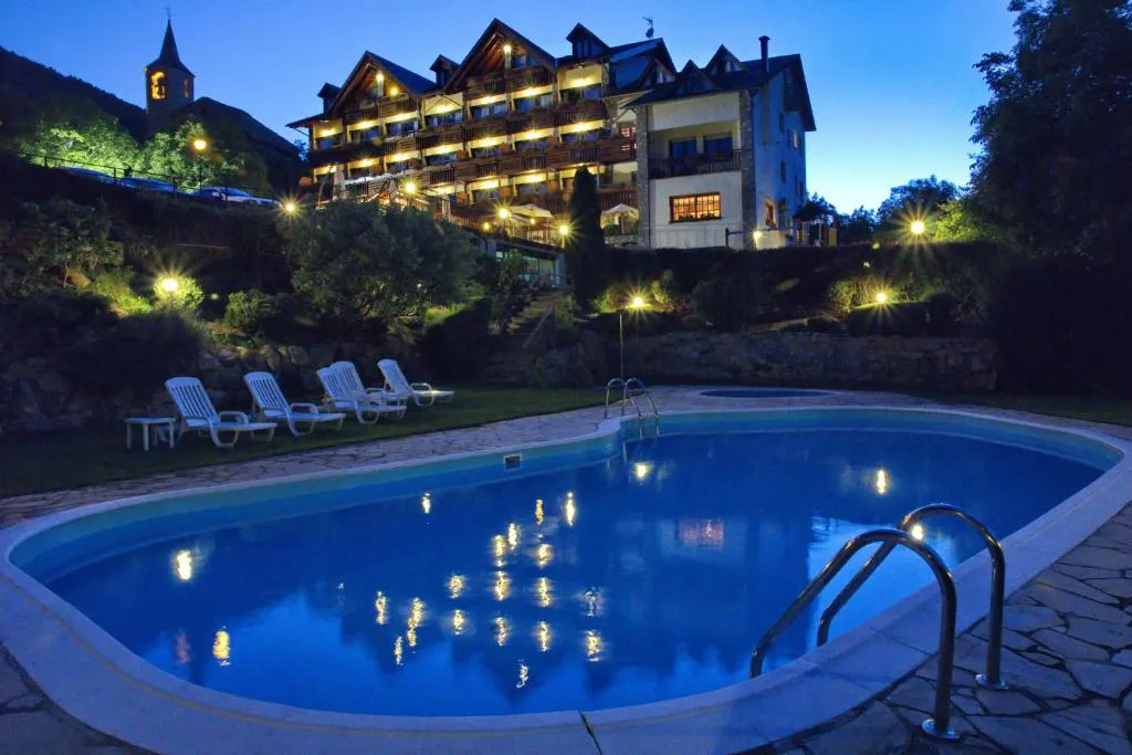 Piscina iluminada al anochecer con el hotel al fondo